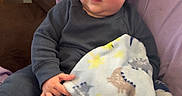 Knox is registered to the contest to win money with this photo: baby, child, infant, blanket, cozy, sitting, indoors, soft_texture, face, foot, clothing, purple, gray_outfit, expression, home_interior, wall_art, furniture, comfort, portrait, cute