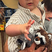 Knox is registered to the contest to win money with this photo: baby, child, cowboy_hat, stuffed_animals, plush_toy, person, indoor, clothing_store, wood_floor, holding, cute, striped_shirt, reaching_hand, adult_arm, portrait, shopping, retail, casual, hat, smiling