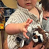 baby, child, cowboy_hat, plush_toy, stuffed_animal, person, indoor, clothing, striped_shirt, hand, face, holding, adult_hand, store, wood_floor, shelf, cute, reaching, portrait, young_child