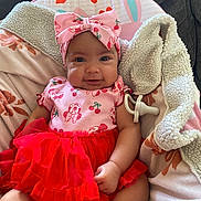 Halo is registered to the contest to win money with this photo: baby, infant, child, headband, bow, red_tutu, pink_outfit, pacifier, blanket, couch, smiling, sitting, portrait, indoor, cute, hand, eyes, cherry_print, bunny_background, cozy