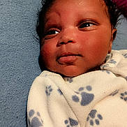 Ja'Ryallen is registered to the contest to win money with this photo: baby, infant, face, blanket, paw_print, curly_hair, blue_background, clothing, closeup, portrait, newborn, soft_lighting, skin, person, indoors, cute, expression, young_child, sleepwear, resting