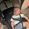 baby, casual_clothing, child, concrete, curious, daylight, expression, footwear, outdoor, person, seatbelt, shade, sitting, stroller, summer, sunlight, toddler, transport, wheel, young_child