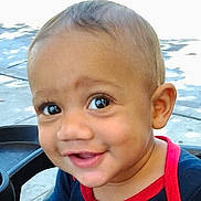 Kyzaiah is registered to the contest to win money with this photo: baby, child, infant, portrait, close_up, smiling, happy, face, eyes, blue_eyes, short_hair, outdoor, daylight, stroller, chair, red_shirt, blue_clothing, person, photography, adorable