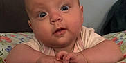 Violetta is registered to the contest to win money with this photo: baby, child, chubby, close_up, colorful, curious, cute, expression, face, floral_pattern, hands, head, indoors, infant, lying_down, person, pillow, skin, wide_eyes, young_child