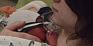 Violetta is registered to the contest to win money with this photo: newborn, baby, woman, blanket, hospital, hat, face, hand, breathing_mask, skin, person, closeup, indoor, mother, care, love, comfort, medical, rest, tenderness