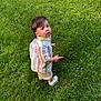 toddler, child, grass, outdoor, curious, striped_shirt, shorts, white_shoes, socks, standing, pointing, greenery, nature, summer, young_child, casual_clothing, daylight, portrait, exploring, lawn