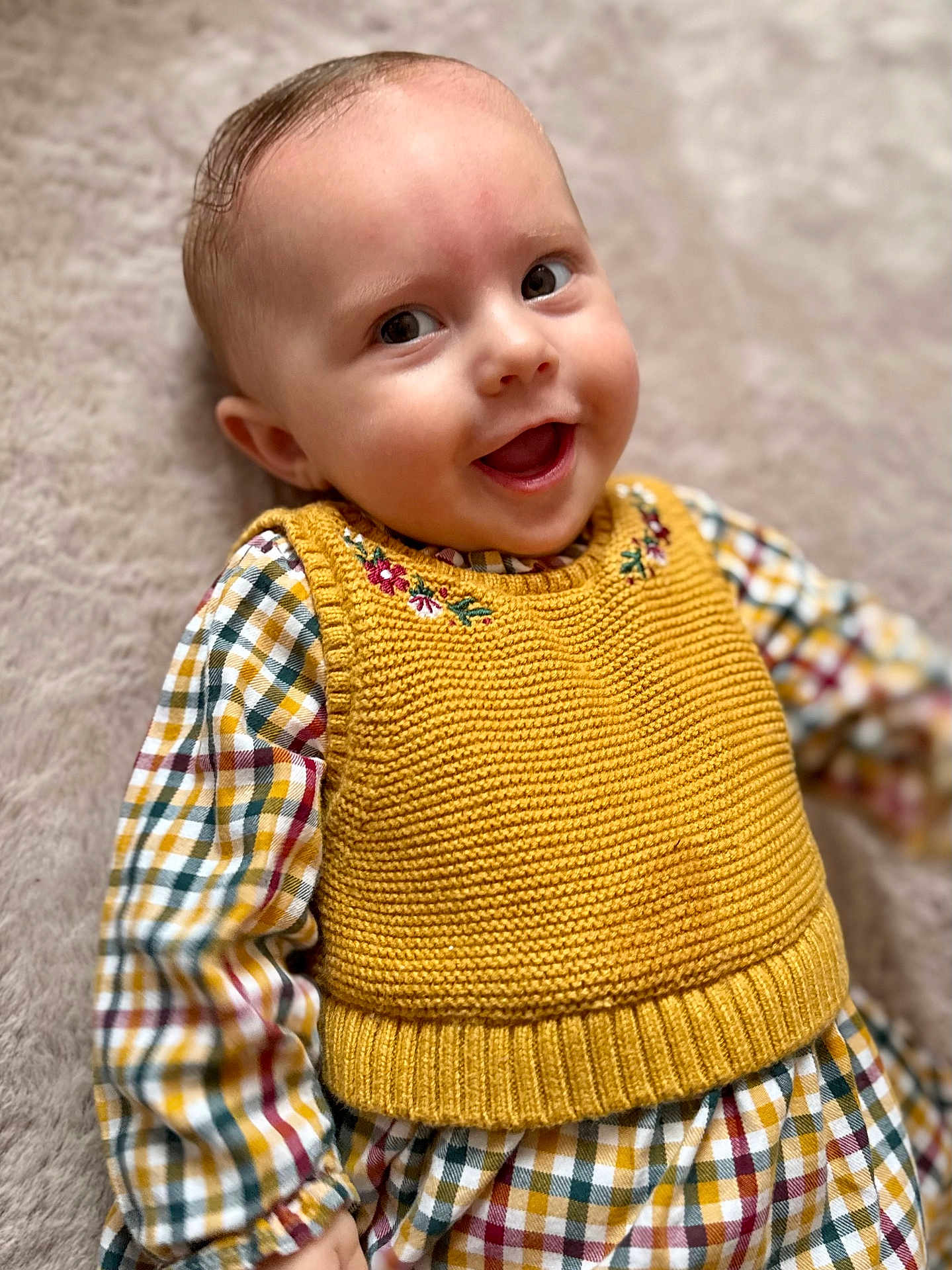 Victoire a rejoint le concours — aidez-le/la à gagner de superbes lots ! baby, smiling, yellow_vest, knitted_clothing, checkered_pattern, happy, infant, cute, child, portrait, soft_texture, lying_down, casual_clothing, indoors, close_up, face, eyes, mouth_open, head, skin