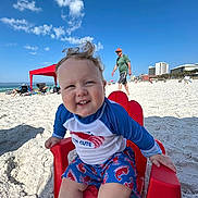 Cohen joined the competition — help win amazing prizes! toddler, beach, child, smiling, red_chair, sand, sunny, blue_sky, clouds, ocean, playing, casual_clothing, outdoor, vacation, happy, person, summer, family, relaxation, fun
