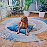 dog, brown_dog, cushion, round_rug, living_room, wooden_floor, plants, potted_plants, table, lamp, window, decor, indoor, relaxed, pet, furniture, calm, cozy, bright, home