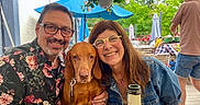 Mila participe au concours pour gagner de l'argent avec cette photo : man, woman, dog, smiling, glasses, outdoor, cafe, table, bottle, glass, umbrella, greenery, flower_pot, casual_clothing, people, happy, leisure, portrait, summer, seating