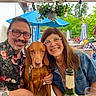 man, woman, dog, smiling, glasses, outdoor, cafe, table, bottle, glass, umbrella, greenery, flower_pot, casual_clothing, people, happy, leisure, portrait, summer, seating