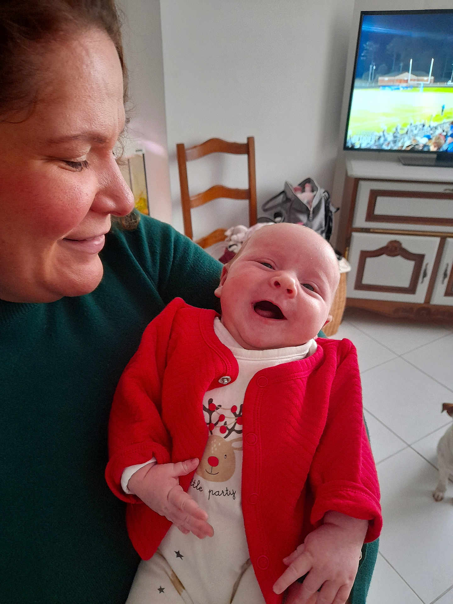 Solyne a rejoint le concours — aidez-le/la à gagner de superbes lots ! baby, adult, smiling, red_cardigan, indoor, chair, television, dog, floor_tiles, cabinet, person, happy, holding, home, furniture, portrait, cute, infant, cozy, family