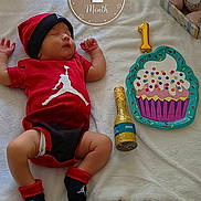Owen is registered to the contest to win money with this photo: baby, infant, newborn, child, sleeping, portrait, birthday, one_month, red_outfit, hat, blanket, stuffed_animals, balloons, cupcake, celebration, bed, indoor, toys, bottle, photography