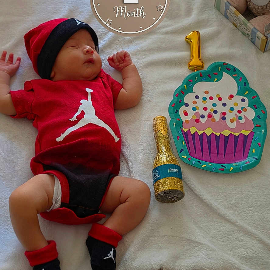 Owen is registered to the contest to win money with this photo: baby, infant, newborn, child, sleeping, portrait, birthday, one_month, red_outfit, hat, blanket, stuffed_animals, balloons, cupcake, celebration, bed, indoor, toys, bottle, photography