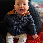 Emerson is registered to the contest to win money with this photo: baby, blanket, child, clothing, cozy, cute, expression, face, happy, indoor, infant, jacket, pants, patterned, person, portrait, sitting, smiling, warm, young