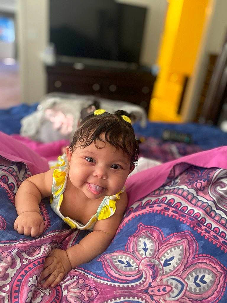 Amoura is registered to the contest to win money with this photo: baby, bed, black_hair, child, comfort, couch, flooring, fun, happy, home_appliance, joy, leisure, magenta, person, pink, purple, room, skin, television, television_set