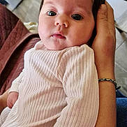 Kamilla a rejoint le concours — aidez-le/la à gagner de superbes lots ! baby, infant, child, person, face, hand, clothing, sleeve, bracelet, indoor, portrait, expression, curious, cozy, ribbed_fabric, adult_hand, closeup, soft_light, blurred_background, skin