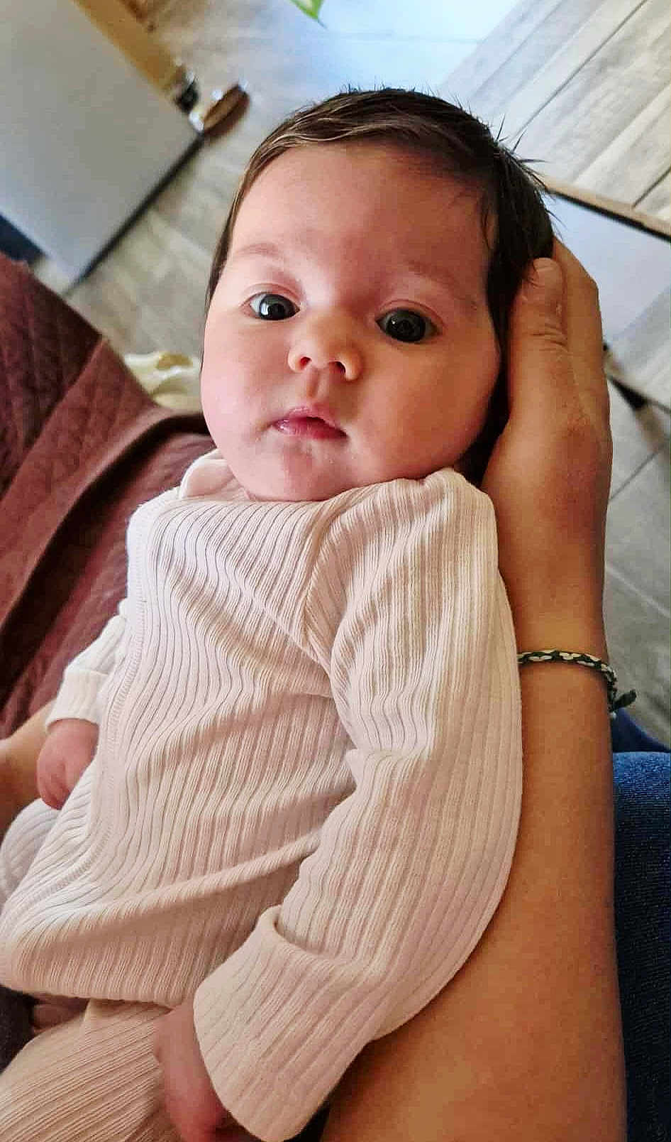 Kamilla a rejoint le concours — aidez-le/la à gagner de superbes lots ! baby, infant, child, person, face, hand, clothing, sleeve, bracelet, indoor, portrait, expression, curious, cozy, ribbed_fabric, adult_hand, closeup, soft_light, blurred_background, skin