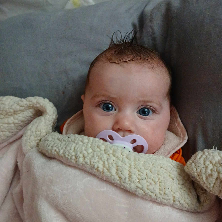 Madlynn is registered to the contest to win money with this photo: baby, blanket, blue_eyes, child, cozy, cute, face, head, indoors, infant, pacifier, person, pillow, portrait, resting, sleepwear, soft_texture, warm, wrapped, young
