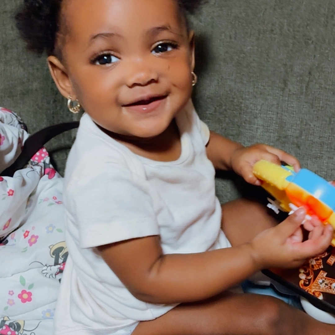 Miyahni is registered to the contest to win money with this photo: toddler, child, smiling, toy, couch, indoor, cute, happy, baby, person, hairstyle, earrings, white_shirt, skin, sitting, playing, furniture, portrait, young_child, casual