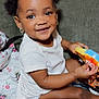 toddler, child, smiling, toy, couch, indoor, happy, hair_puffs, earrings, white_shirt, skin, person, baby, sitting, play, cute, face, bright_eyes, holding, home