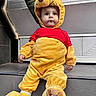 Kenan participe au concours pour gagner de l'argent avec cette photo : baby, child, costume, winnie_the_pooh, yellow, red, plush, toddler, cute, sitting, step, clothing, footwear, indoor, person, face, wide_eyes, hand, support, tile
