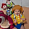 baby, child, toy_story, woody_costume, buzz_lightyear, jessie, lotso, plush_toy, smiling, happy, indoor, tile_floor, cardboard_box, costume, person, cute, holding_object, colorful, playful, portrait