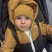 Kenan participe au concours pour gagner de l'argent avec cette photo : baby, child, face, hat, knit_hat, puffer_jacket, jacket, stroller, seatbelt, straps, winter_clothing, outerwear, portrait, infant, cute, indoor, looking_up, young_child, warm_clothing, person