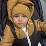 baby, child, face, hat, knit_hat, puffer_jacket, jacket, stroller, seatbelt, straps, winter_clothing, outerwear, portrait, infant, cute, indoor, looking_up, young_child, warm_clothing, person