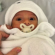 Hector participe au concours pour gagner de l'argent avec cette photo : baby, infant, pacifier, white_towel, hood, hand, close_up, wrapped, cute, soft_texture, blanket, newborn, face, skin, portrait, indoors, comfort, child, person, cozy