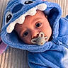 adorable, baby, baby_clothes, blue_onesie, child, costume, cute, expression, eyes, face, headwear, hooded_clothing, indoors, infant, lying_down, pacifier, plush_texture, portrait, soft_fabric, stitch_costume