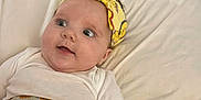 Melody joined the competition — help win amazing prizes! baby, infant, headband, yellow, white_clothing, cushion, bed, soft_fabric, face, eyes, expression, child, indoors, comfort, resting, portrait, cute, small_person, laying_down, clothing