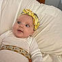 baby, infant, headband, yellow, white_clothing, cushion, bed, soft_fabric, face, eyes, expression, child, indoors, comfort, resting, portrait, cute, small_person, laying_down, clothing