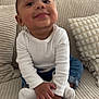 toddler, child, smiling, white_shirt, blue_jeans, sitting, couch, cushion, home, indoors, hands, feet, white_socks, face, cute, happy, portrait, young_child, cozy, casual_clothing