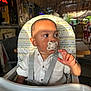 toddler, child, pacifier, high_chair, white_shirt, indoor, sunlight, patterned_cushion, curious, seatbelt, restaurant, table, hand, face, portrait, brown_skin, short_hair, baby, casual, daylight