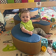 Ezra joined the competition — help win amazing prizes! baby, child, green_bib, blue_cushion, tan_cushion, toys, colorful, playmat, mirror, reflection, indoor, smiling, seated, soft_furniture, playroom, cute, happy, infant, floor_mat, patterned_mat