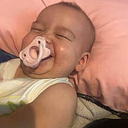 Amor is registered to the contest to win money with this photo: baby, pacifier, smile, happy, child, pillow, blanket, infant, face, skin, arm, cute, sleeping_area, indoors, cozy, comfort, joy, expression, toddler, clothing