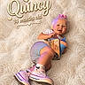 Quincey is registered to the contest to win money with this photo: baby, child, infant, sitting, blanket, toy, sippy_cup, shoes, socks, pink_bow, hair, face, smile, clothing, phone_case, indoor, portrait, cute, happy, soft_texture