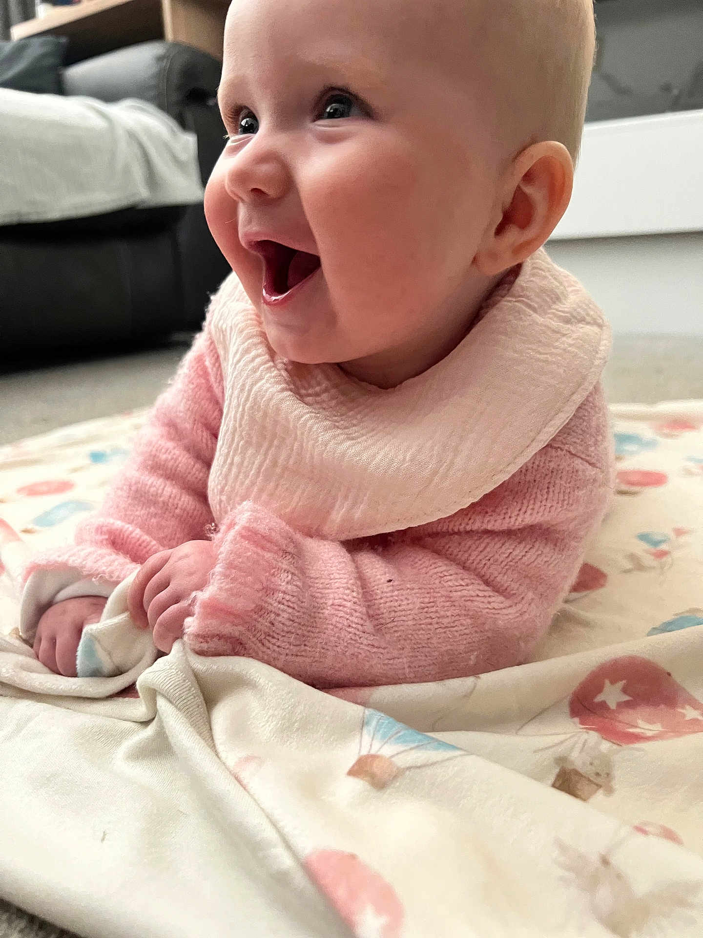 Millie joined the competition — help win amazing prizes! baby, infant, smiling, pink_sweater, bib, blanket, indoor, happy, cute, child, face, hands, lying_down, soft_toys, cozy, pattern, mouth_open, expression, skin, young