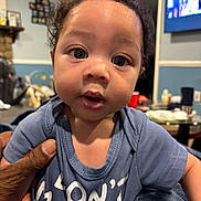 Kahmari is registered to the contest to win money with this photo: baby, blue_shirt, casual, child, close_up, curly_hair, cute, expression, eyes, face, furniture, hand, home, indoor, living_room, person, portrait, skin, television, young_child