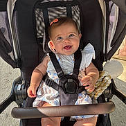 Adèle a rejoint le concours — aidez-le/la à gagner de superbes lots ! baby, smiling, stroller, child, toy, sunlight, happy, cute, infant, clothing, hair_clip, seatbelt, outdoor, sitting, person, portrait, baby_dress, footwear, playful, daylight