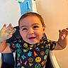 baby, child, toddler, birthday, crown, party_hat, smiling, happy, portrait, sitting, high_chair, indoors, colorful, clothing, patterned_shirt, hands_up, celebration, face, dark_hair, photography