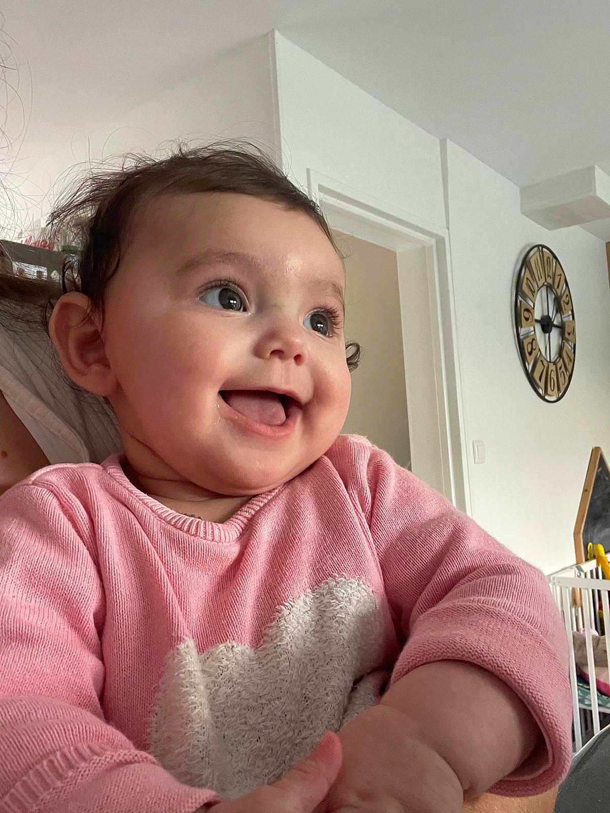 Tiana a rejoint le concours — aidez-le/la à gagner de superbes lots ! baby, child, smiling, pink_sweater, heart_pattern, indoor, face, happy, cute, portrait, closeup, person, infant, long_sleeve, skin, head, hand, home, clock, wall