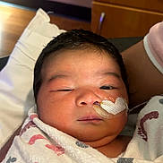 Ailanny is registered to the contest to win money with this photo: newborn, baby, infant, face, portrait, sleepy, hospital, blanket, swaddled, medical_tube, tape, cheek, dark_hair, eyes, nose, mouth, bed, pillow, adult_arm, indoor