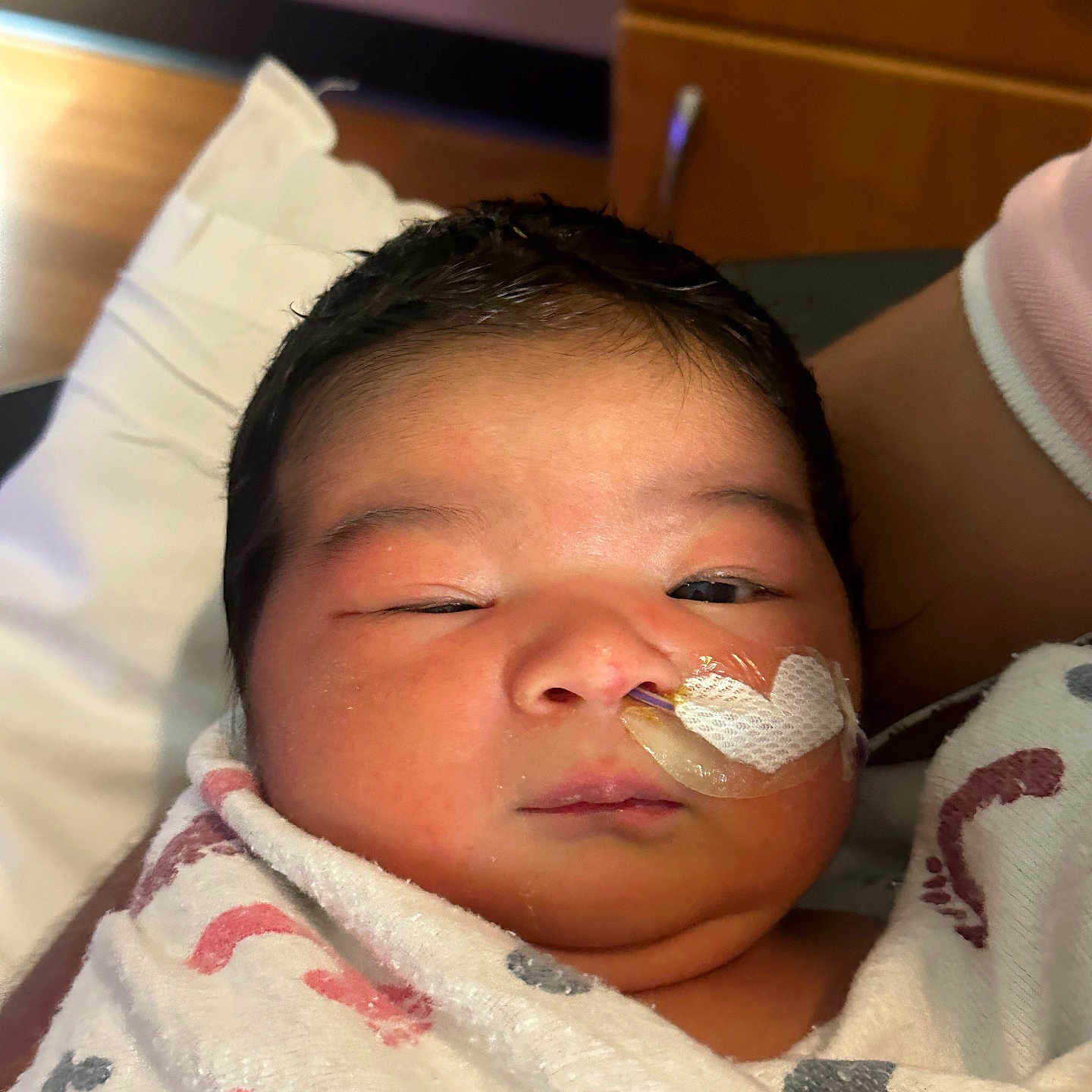 Ailanny is registered to the contest to win money with this photo: newborn, baby, infant, face, portrait, sleepy, hospital, blanket, swaddled, medical_tube, tape, cheek, dark_hair, eyes, nose, mouth, bed, pillow, adult_arm, indoor