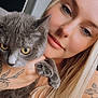 woman, cat, blonde_hair, tattoo, gray_cat, yellow_eyes, close_up, selfie, portrait, indoor, holding, pet, animal, face, long_hair, skin, expression, person, cute, feline