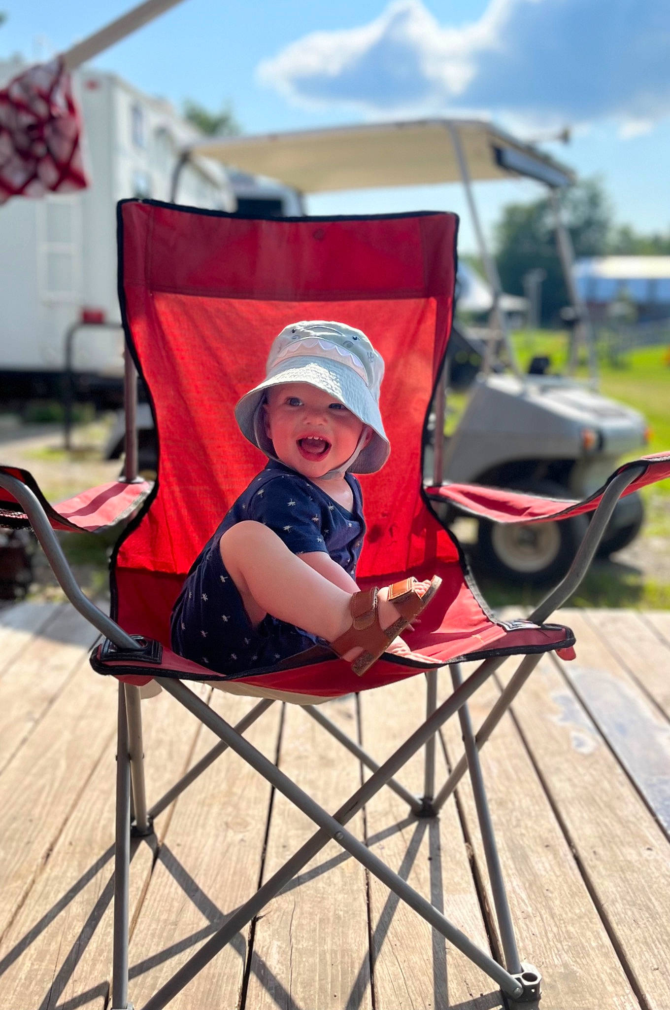 Layne is registered to the contest to win money with this photo: baby, baby_products, baby_toddler_clothing, chair, child, cloud, comfort, event, folding_chair, fun, grass, hat, headwear, leisure, person, recreation, red, sitting, sky, sun_hat