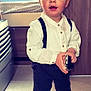 Blueboy a rejoint le concours — aidez-le/la à gagner de superbes lots ! toddler, child, boy, indoors, white_shirt, suspenders, dark_pants, black_shoes, holding_brush, curious_expression, blue_eyes, short_hair, carpet, bed, furniture, wooden_panel, floor, standing, person, portrait