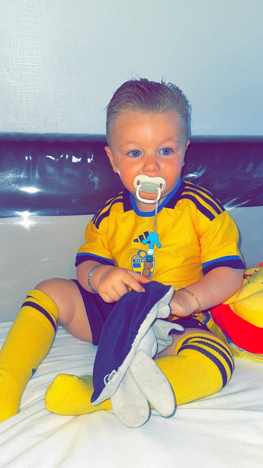 Blueboy a rejoint le concours — aidez-le/la à gagner de superbes lots ! toddler, child, pacifier, yellow_socks, yellow_shirt, blue_stripes, plush_toy, sitting, indoors, white_background, bracelet, blue_eyes, shorts, hair_slicked_back, toy, cute, portrait, baby, sportswear, couch