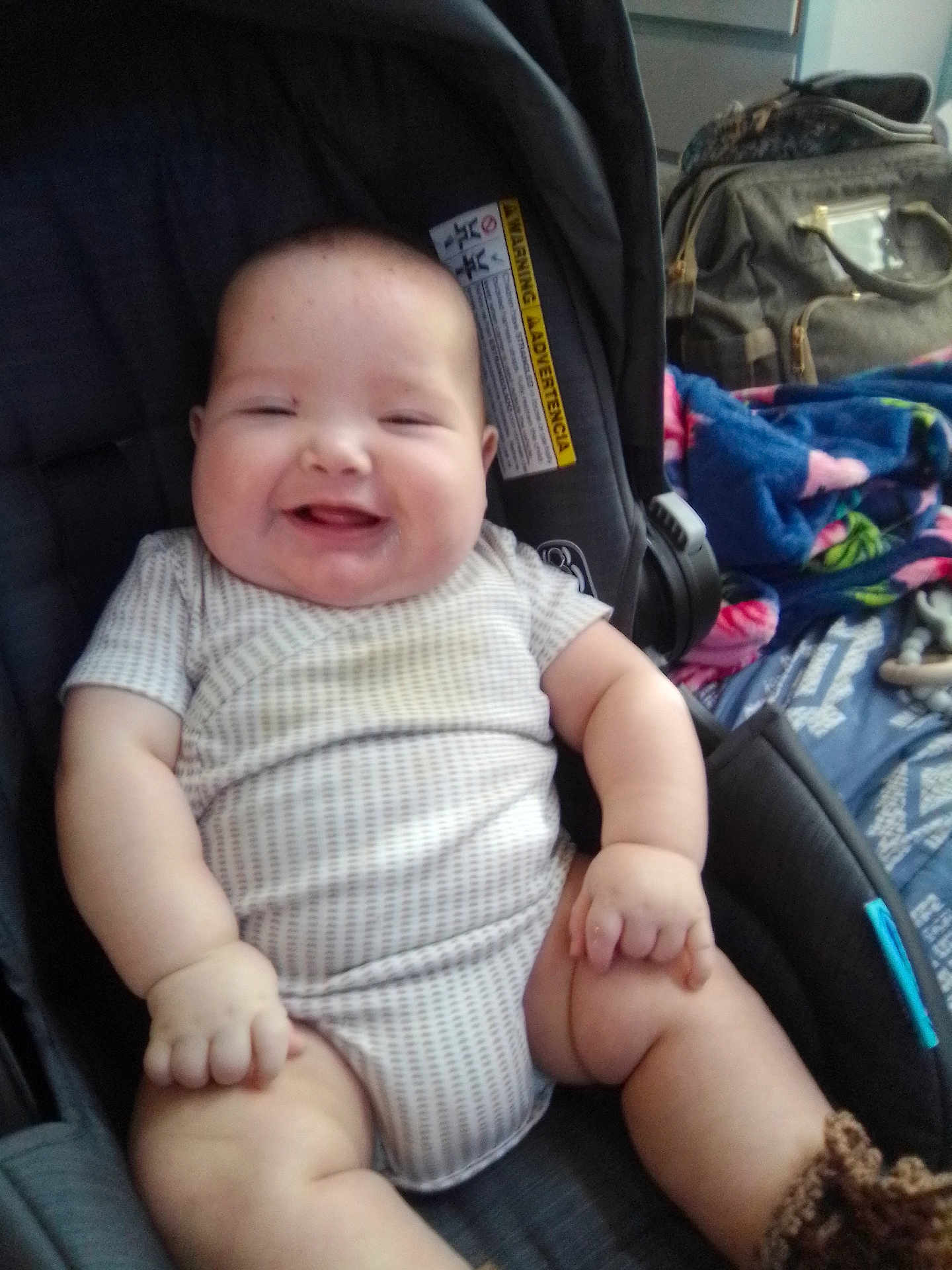 Braik is registered to the contest to win money with this photo: baby, infant, smiling, car_seat, onesie, chubby, cheeks, hands, legs, blanket, backpack, buckle, seat_pad, portrait, indoors, happy, clothing, plush_blanket, diaper, sitting